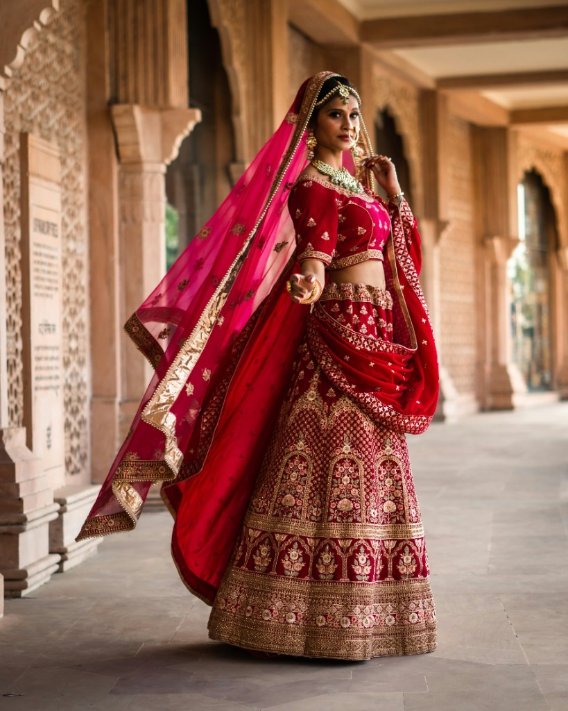 A bride in a red and gold lehenga standing in a palace corridor