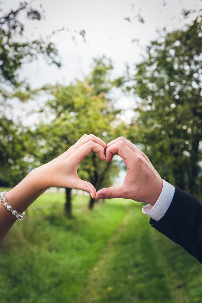 Two hands forming a heart against a green garden